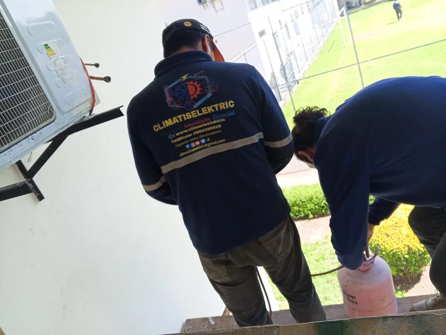 Dos técnicos cargando refrigerante a un equipo de aire acondicionado