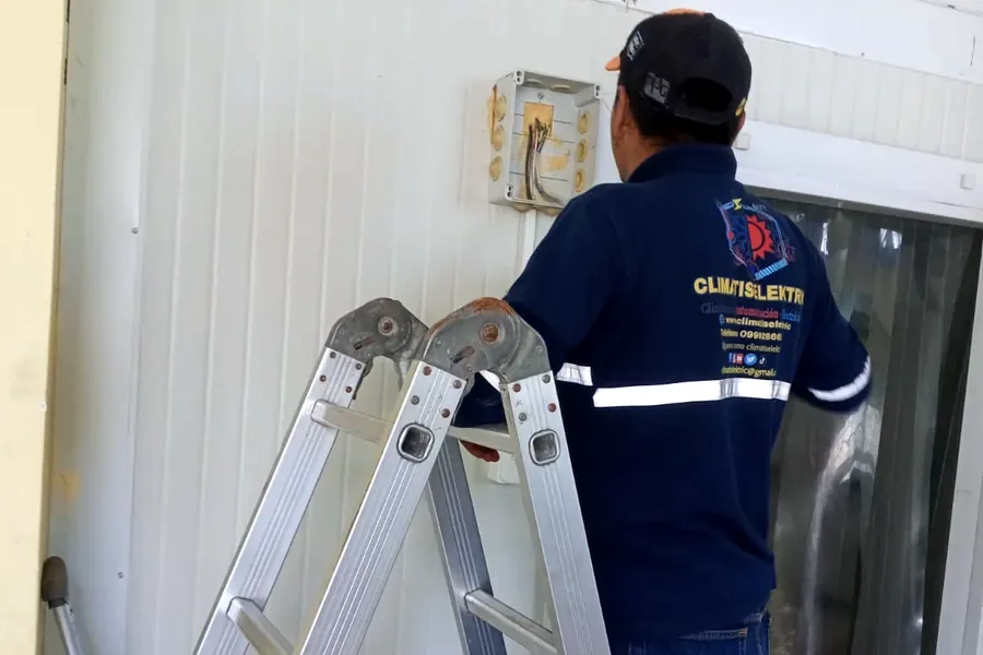 Técnico de Climatiselektric sobre una escalera revisando una caja eléctrica